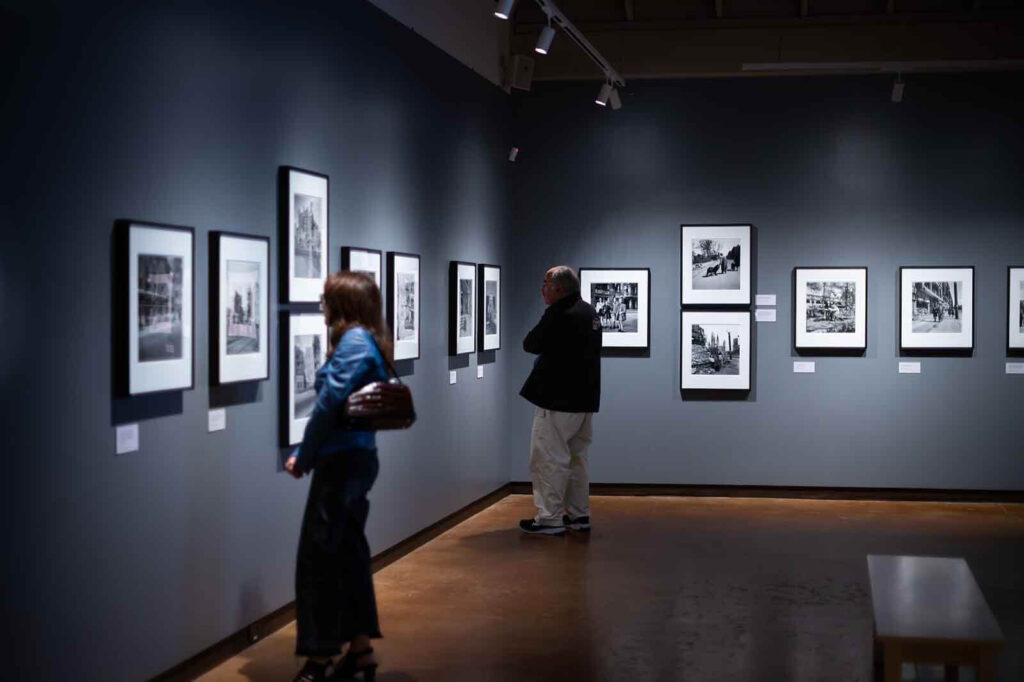 2 people standing in gallery looking at framed photographs on the wall