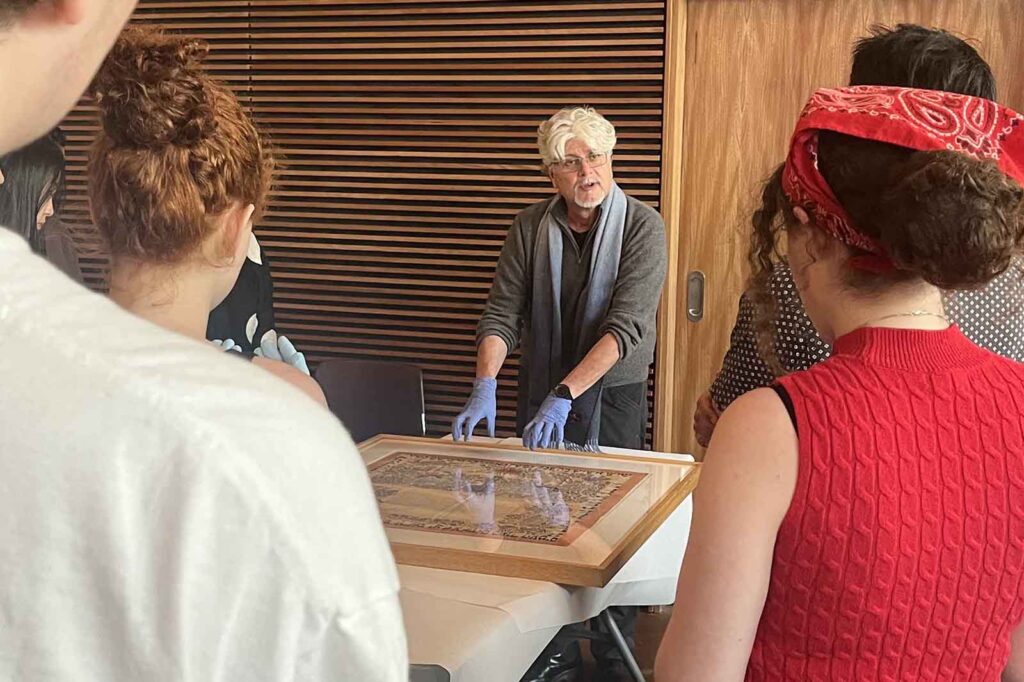 Man speaking about framed manuscript with students looking on