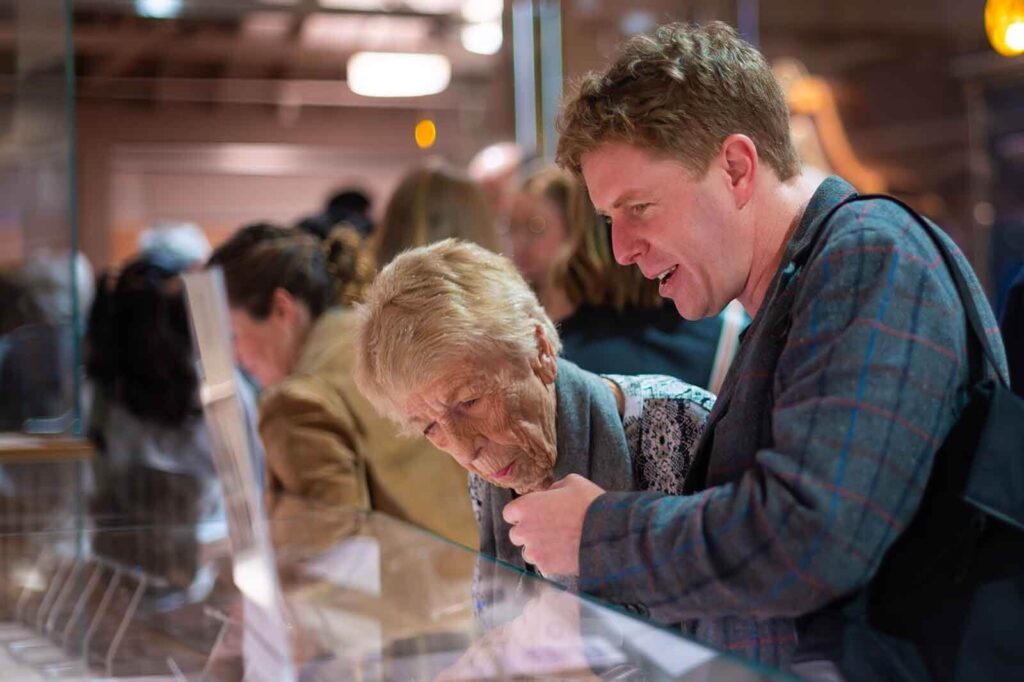 older woman and younger man looking at display case in exhibition