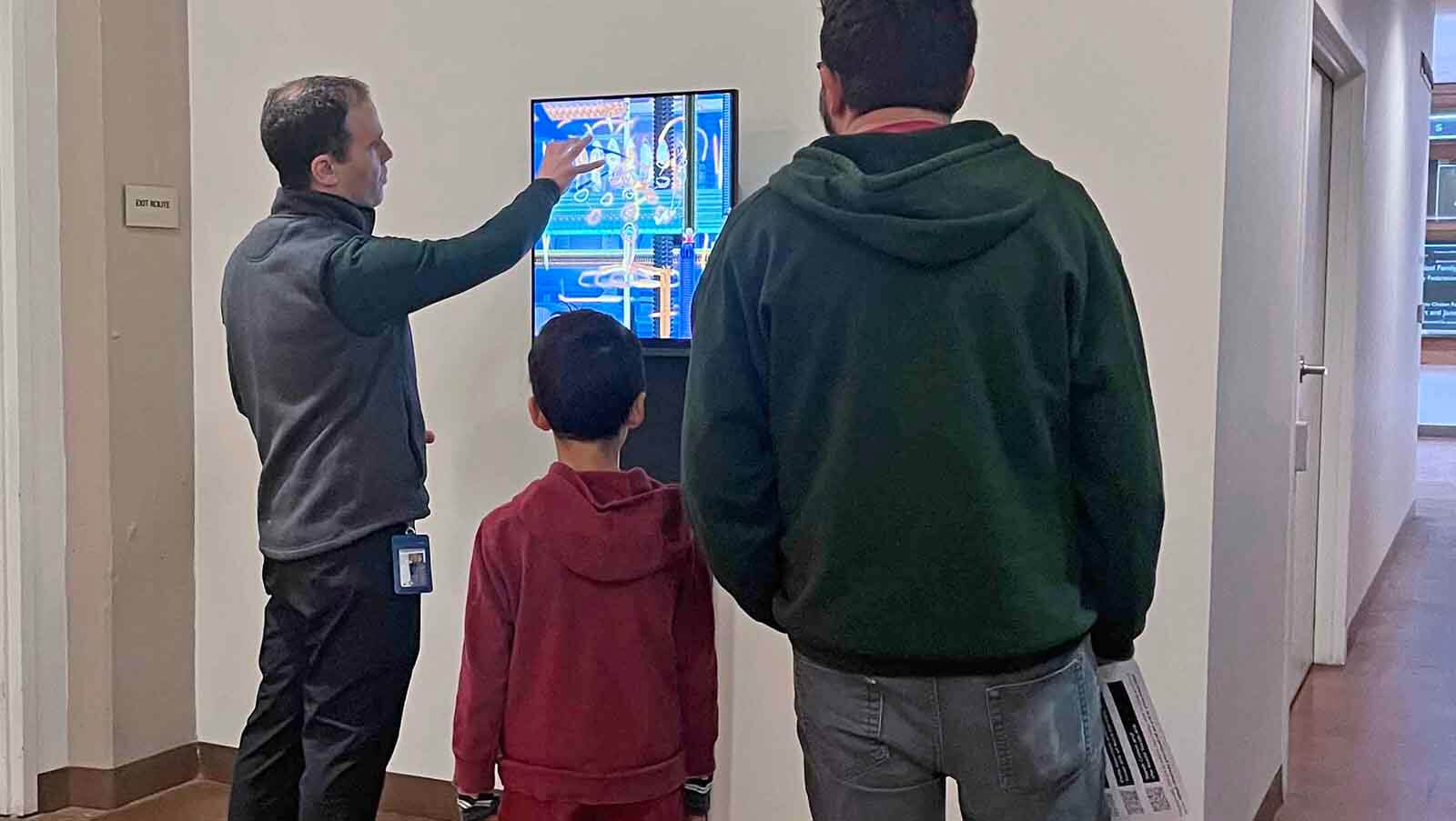 2 adults and a child looking at a screen with artwork
